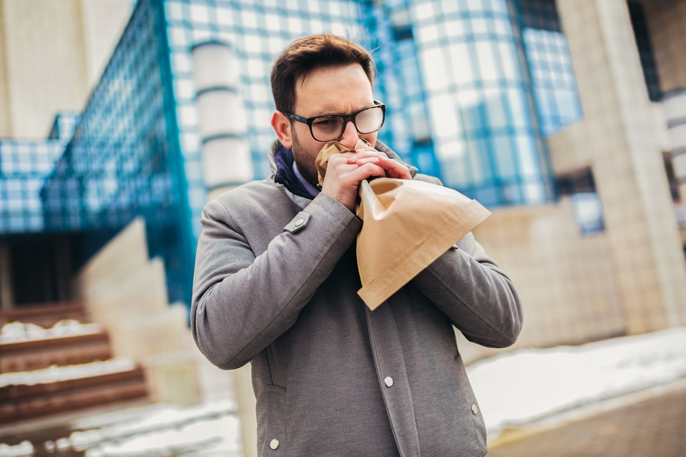 Man holding paper bag over mouth as if having a panic attack