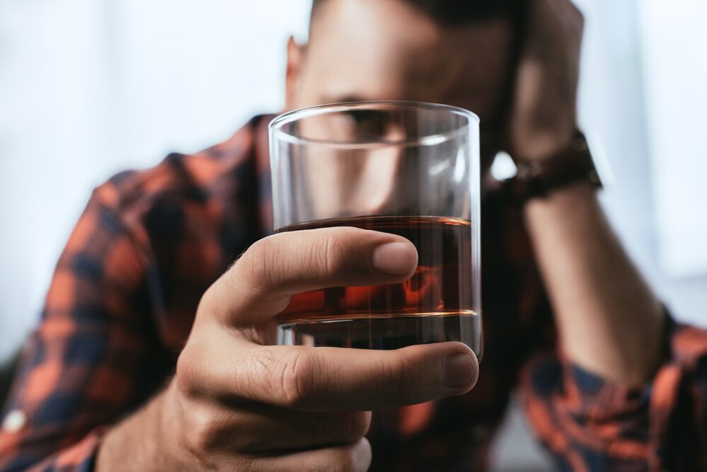 man having an addiction relapse holding a glass of alcohol