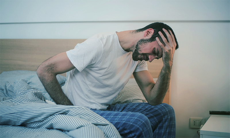 1_BHC_Blog_LiverDamageFromAlcohol_FATIGUE2 a man bent over in pain, sitting on his bed.